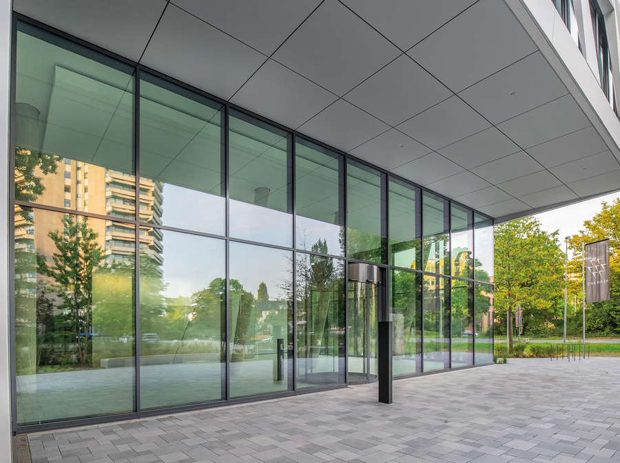Entrance area of ONE PLAZA with a spacious glass façade, modern architecture, and views of the surrounding buildings and green spaces.